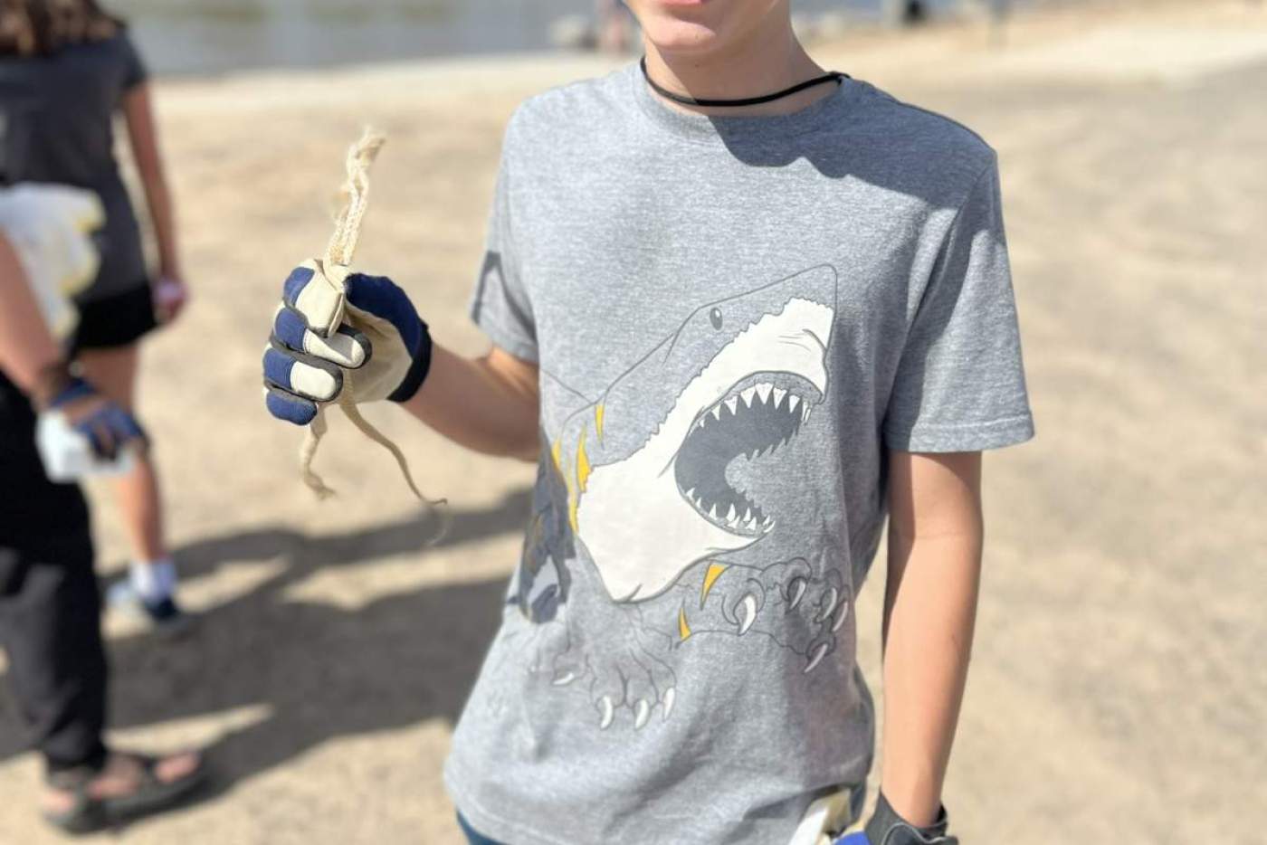 boy wearing gloves holds trash that he's collected next to a river