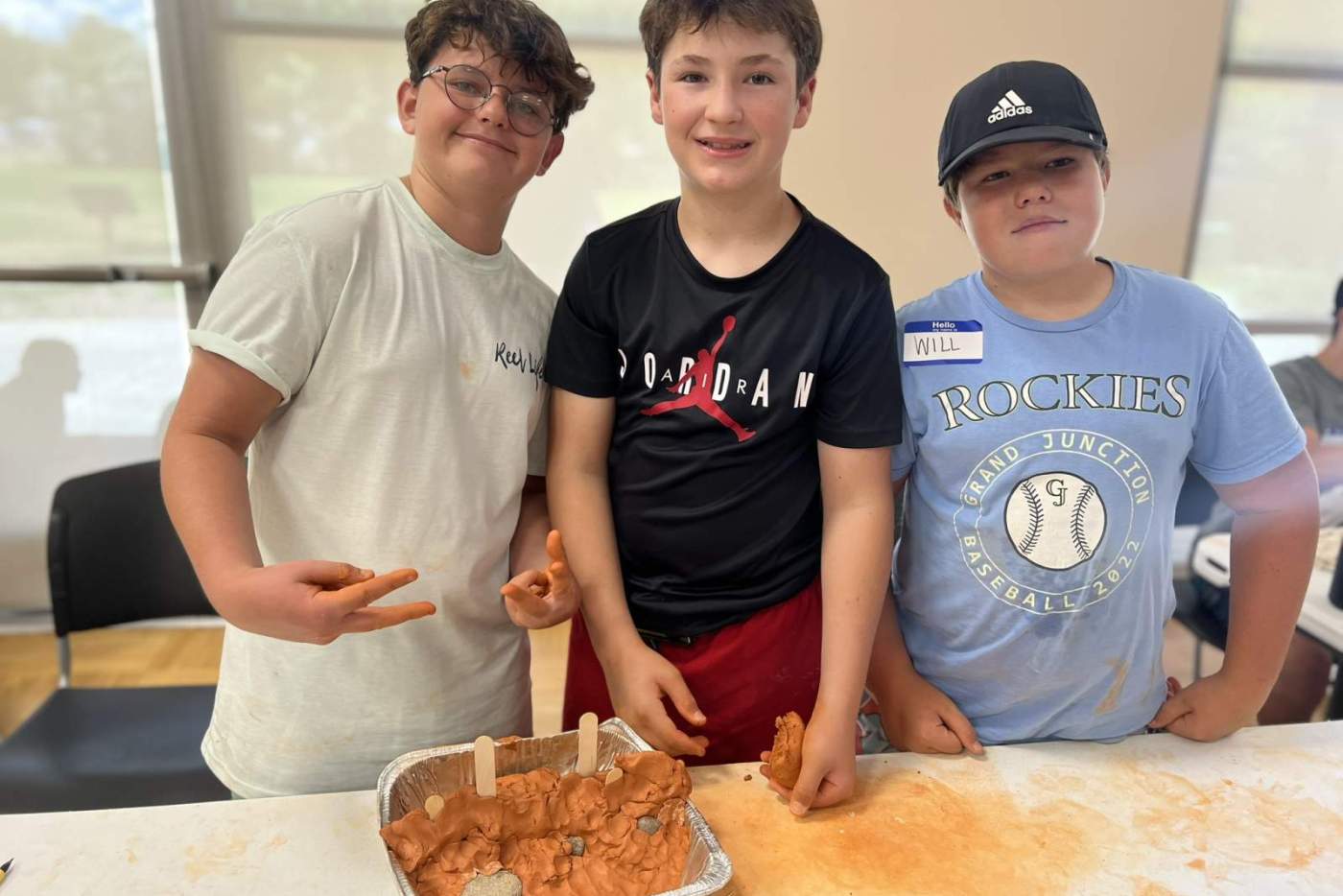 3 boys pose with their metal tray holding clay dam model