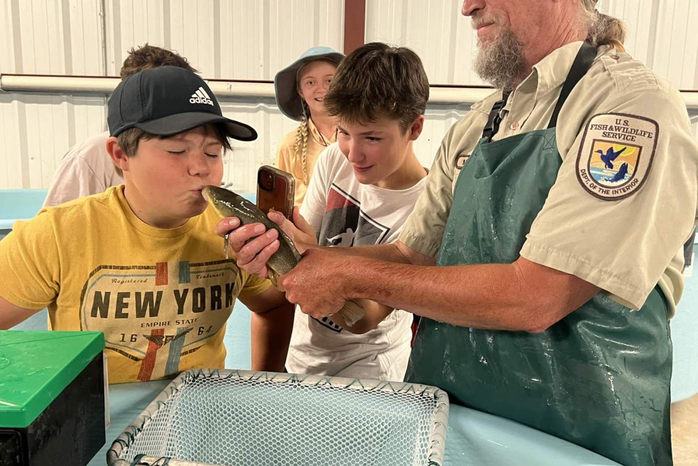 boy kisses a fish held by man in a hat and apron