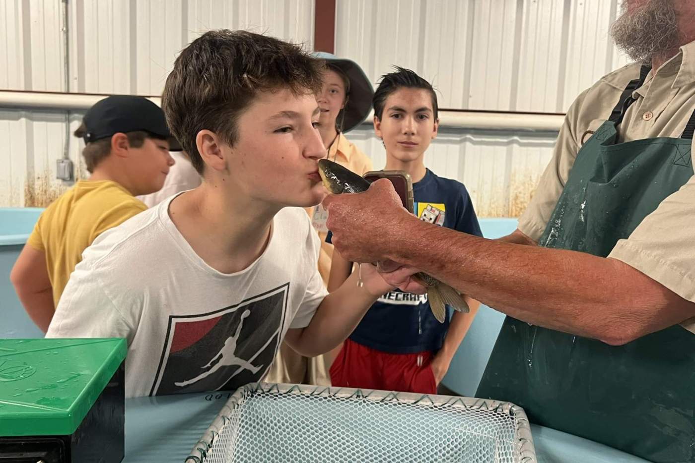 boy kisses a fish held by man in a hat and apron