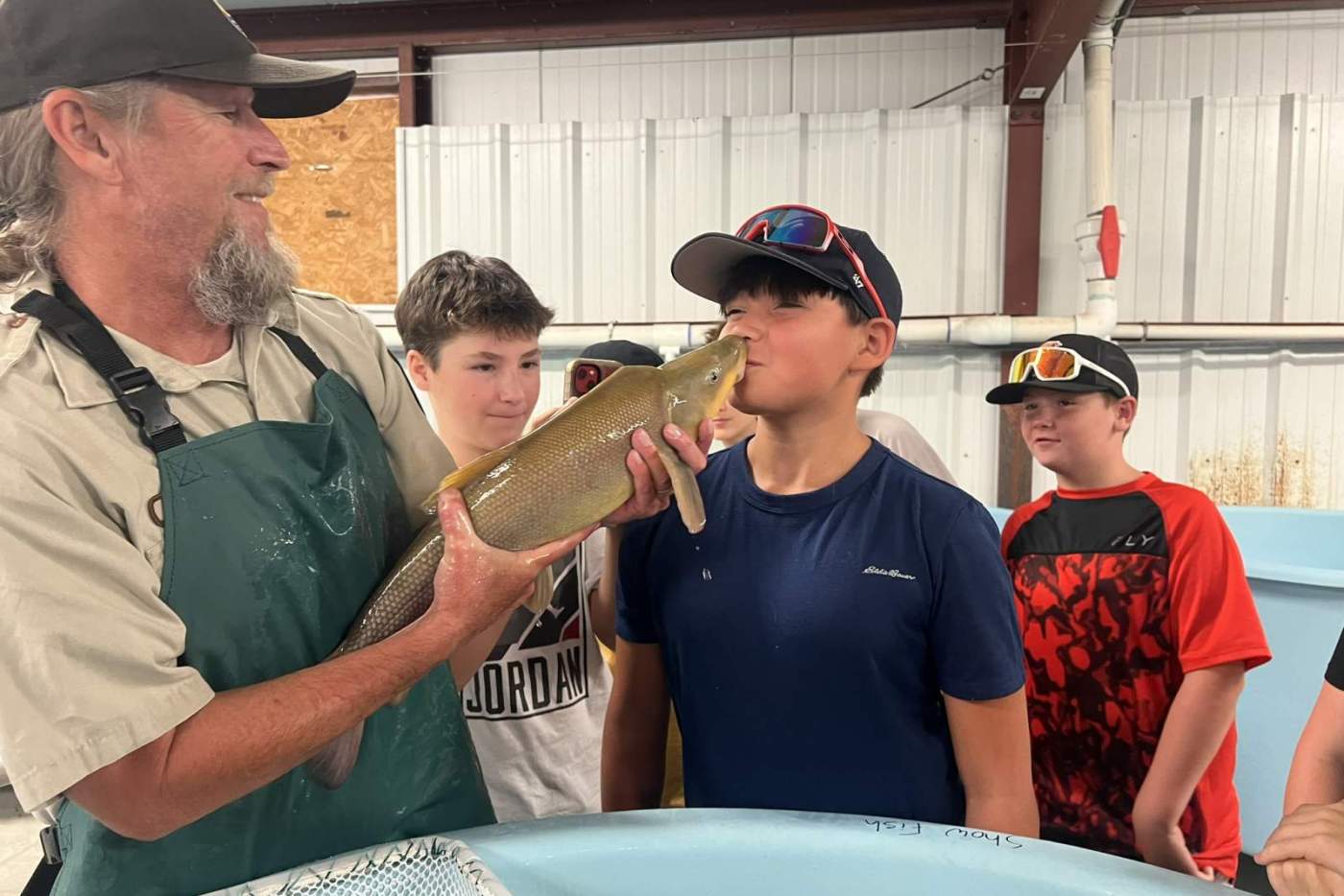 boy kisses a fish held by man in a hat and apron