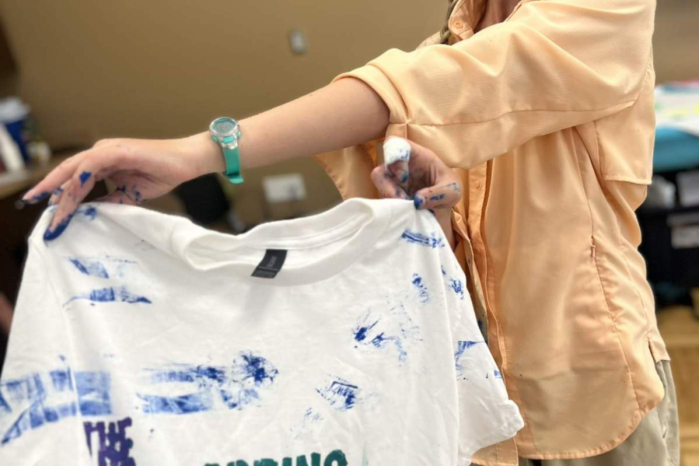 girl holds shirt she designed that says "The Wellspring Project"