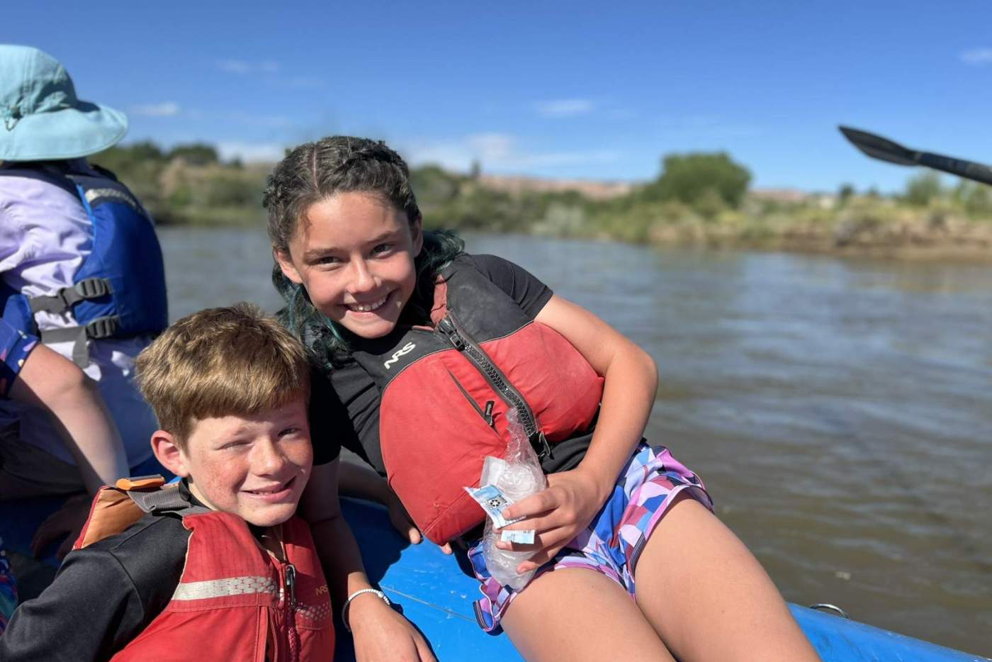 boy and girl in red life vests pose for a photo together on a blue raft in the river