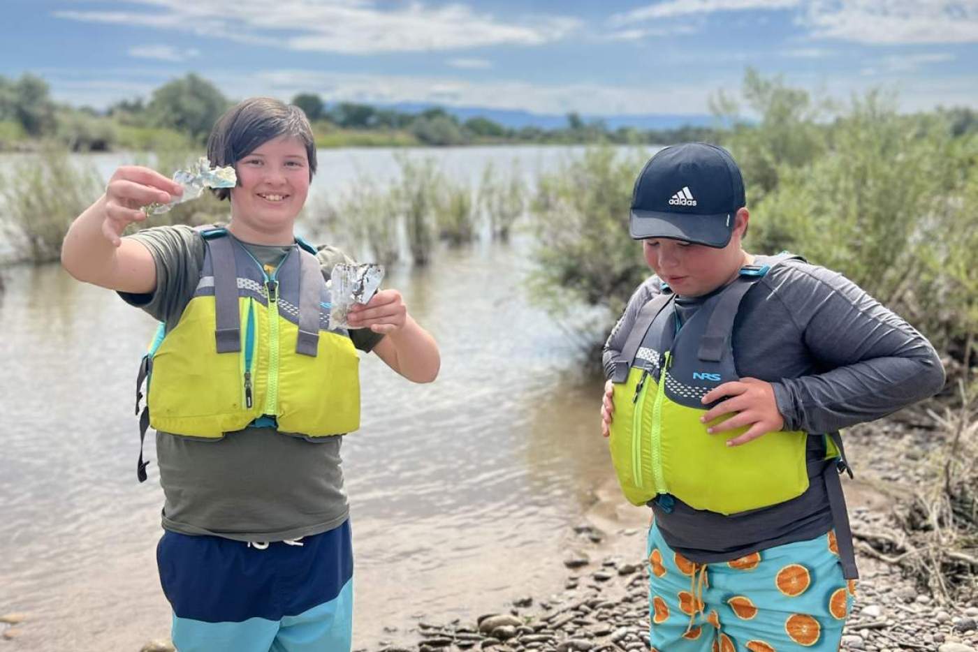 2 boys in yellow life vests standing on rocky riverside