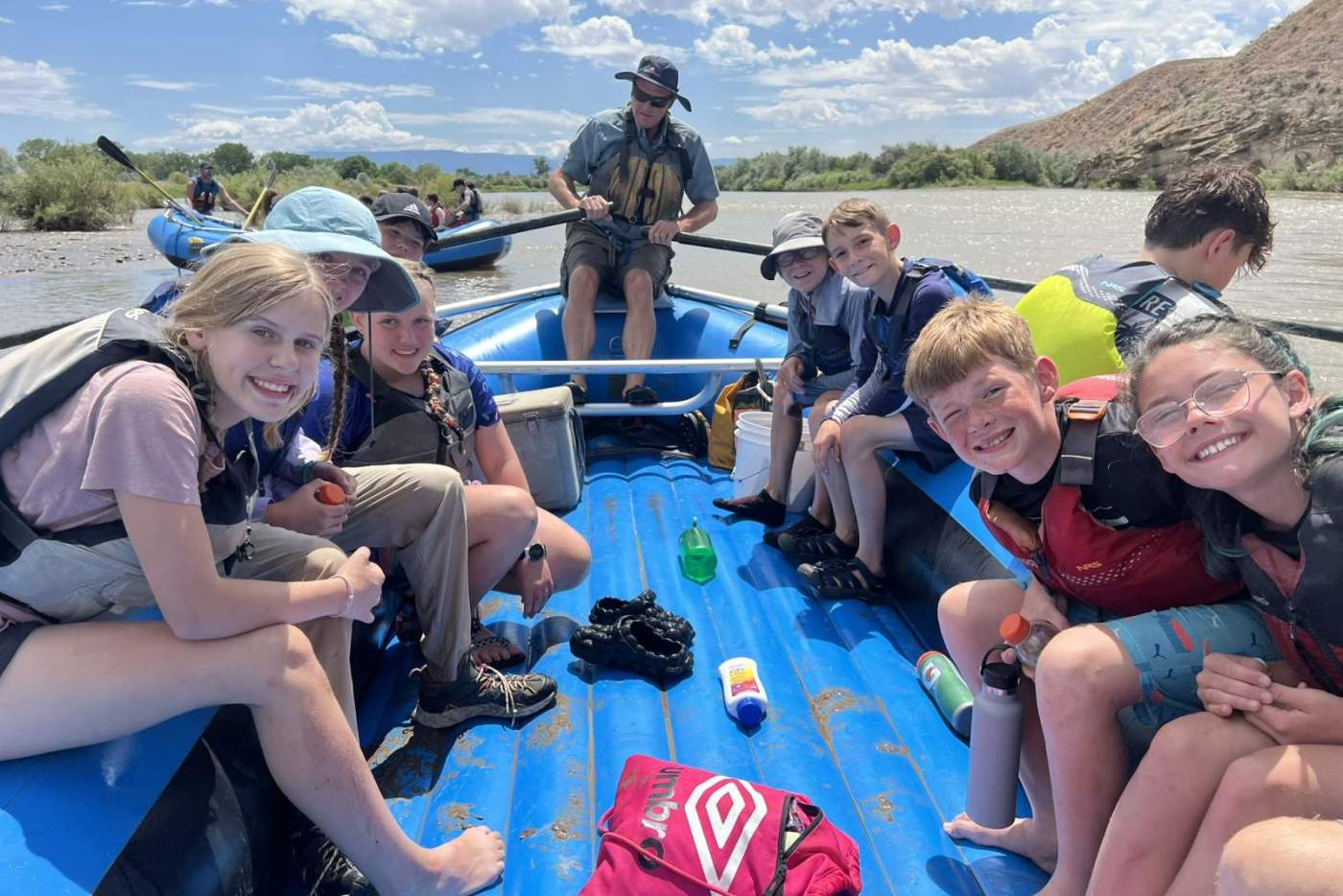 group of smiling middle school students in life vests sitting on a raft floating down the river