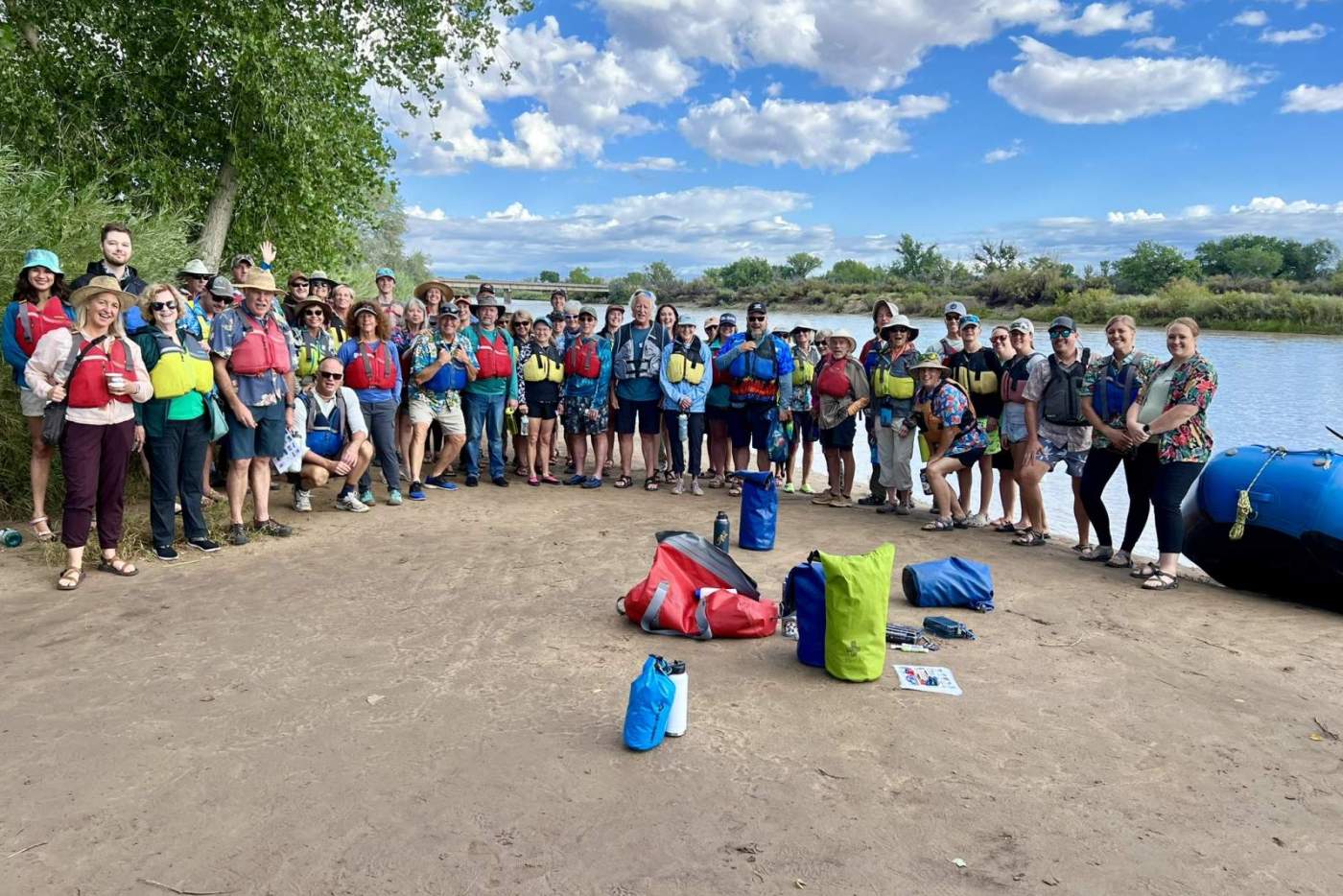 large group of people in life vests pose by the riverside for a group photo