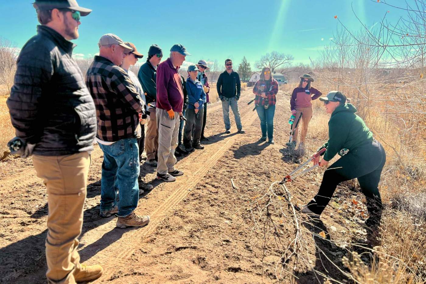 group of volunteers stand on dirt road listening to woman explain tasks