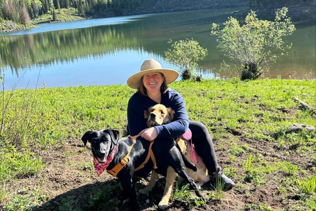 Woman sitting in front of a mountain lake with 2 dogs